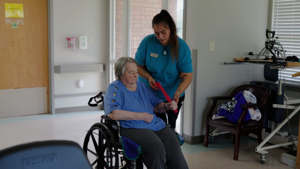A woman in a wheelchair is going through physical therapy with a nurse at a short term care facility