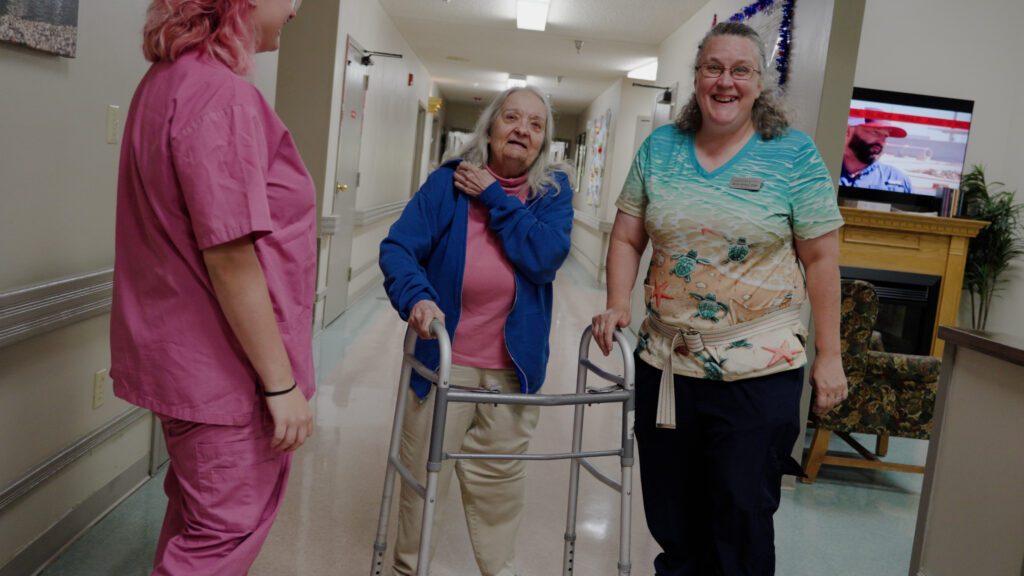 A nurse and a resident walking down a hallway smiling and talking in a skilled nursing home