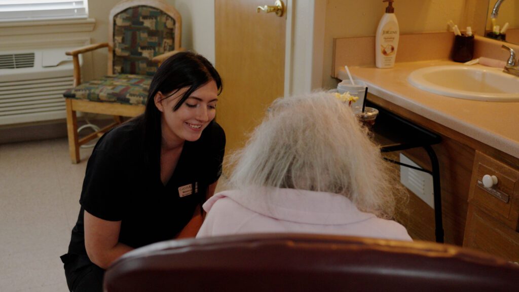 A nurse and a memory care resident talk and smile at a skilled nursing facility