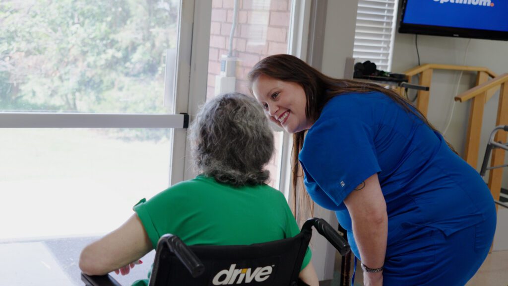 A nurse smiles at a woman in a wheelchair at a skilled nursing facility